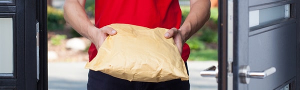 Eine Person in einem roten Hemd hält einen gepolsterten Umschlag oder ein Paket und steht in einer Tür.