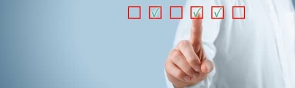 Eine Person zeigt auf eine Reihe von fünf Checklistenfeldern, die alle mit grünen Häkchen markiert sind. Der Hintergrund ist hellblau.