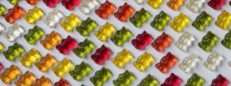 Reihen verschiedener bunter Gummibärchen, ordentlich aufgereiht auf einer weißen Oberfläche.