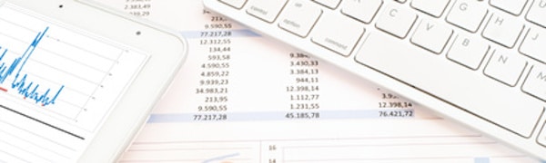 Auf dem Bild sind ein Tablet mit einem Diagramm, eine Tastatur und Dokumente mit Finanzdaten zu sehen.