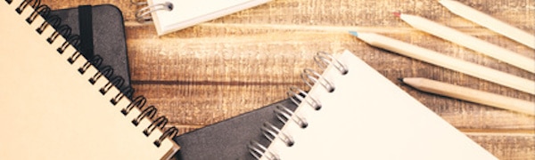 Eine Sammlung von Spiralblöcken und mehreren Buntstiften sind auf einer Holzoberfläche angeordnet.