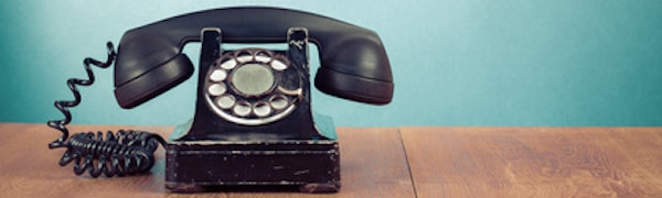 Ein altes Telefon mit Wählscheibe steht auf einer Holzoberfläche vor einem blaugrünen Hintergrund.