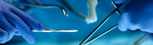 Nahaufnahme der behandschuhten Hände eines Chirurgen, der chirurgische Instrumente über einem blauen Operationstisch hält.