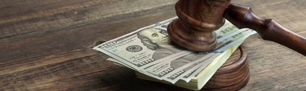 Ein hölzerner Hammer ruht auf einem Stapel Hundert-Dollar-Scheine auf einer Holzoberfläche.