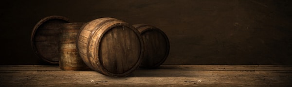 Mehrere Holzfässer stehen auf einem Holzboden vor braunem Hintergrund.