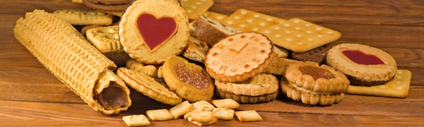 Verschiedene Kekse und Plätzchen, darunter herzförmige und runde Kekse mit Füllung aus roter Marmelade, angeordnet auf einer Holzoberfläche.