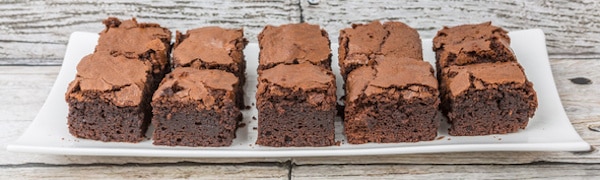 Ein weißer rechteckiger Teller mit zwei Reihen Schokoladenbrownies, die gleichmäßig auf einer hellen Holzoberfläche angeordnet sind.