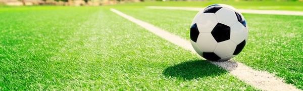 Ein schwarz-weißer Fußball liegt auf einem grünen Feld in der Nähe einer weißen Linie.