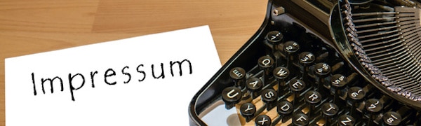 Eine Schreibmaschine mit Papier, auf dem das Wort „Impressum“ steht, auf einem Holzschreibtisch.