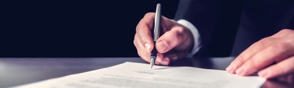 Eine Person unterschreibt ein Dokument mit einem Stift auf einem Schreibtisch.