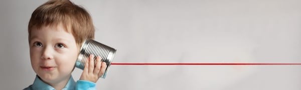 Ein Kind hält eine Blechdose ans Ohr und lauscht einem daran befestigten roten Faden. So wird ein einfaches Kommunikationskonzept veranschaulicht.