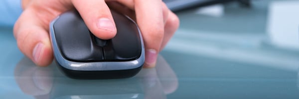 Nahaufnahme der Hand einer Person, die eine schwarze Computermaus auf einer Glasoberfläche benutzt.