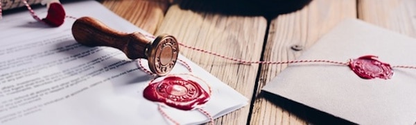 Ein Wachssiegelstempel und rote Wachssiegel auf einem Dokument und einem Umschlag auf einem Holztisch.