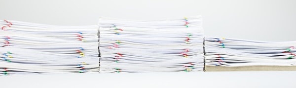 Stapel weißer Papierdokumente, mit bunten Büroklammern gebunden und in Reihen vor einem einfarbigen Hintergrund angeordnet.