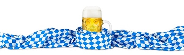 Ein mit schaumigem Bier gefüllter Bierkrug ist von einem blau-weiß karierten Tuch auf weißem Hintergrund umgeben.