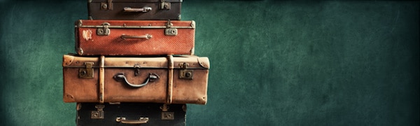 Ein Stapel aus vier Vintage-Koffern in unterschiedlichen Größen und Farben vor einem dunkelgrünen Hintergrund.