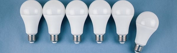 Sechs weiße LED-Glühbirnen mit silbernem Sockel sind in einer Reihe vor blauem Hintergrund zu sehen. Eine Glühbirne ganz rechts ist schräg gestellt.