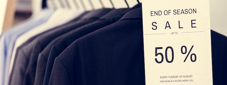 Nahaufnahme eines Ständers mit Hemden. Auf dem Hemd im Vordergrund ist ein Schild mit dem Hinweis auf einen Saisonschlussverkauf mit Rabatten von bis zu 50 % angebracht.