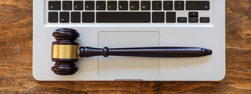 Ein Holzhammer ruht auf dem Touchpad eines geöffneten Laptops auf einer Holzoberfläche.