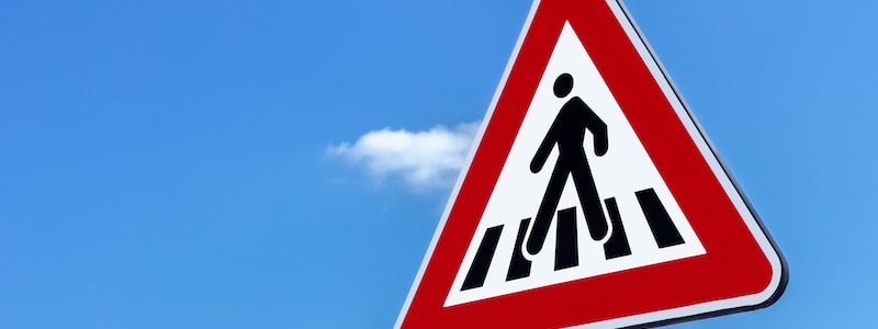 Nahaufnahme eines Fußgängerüberweg-Schildes vor einem klaren blauen Himmel mit einer einzelnen kleinen Wolke.