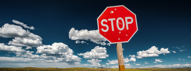 Vor dem Hintergrund eines klaren blauen Himmels mit vereinzelten weißen Wolken steht ein rotes, achteckiges Stoppschild.