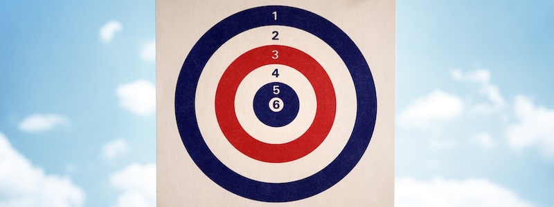 Ein Ziel mit konzentrischen Kreisen in den Farben Blau, Rot und Weiß, wobei jeder Kreis von eins bis sechs nummeriert ist, wird vor dem Hintergrund eines blauen Himmels mit weißen Wolken angezeigt.