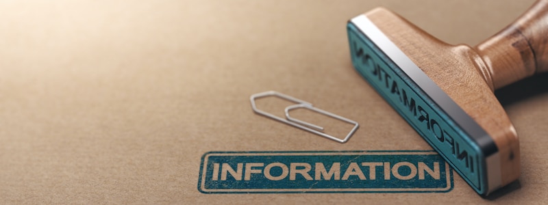 Ein Holzstempel mit der Aufschrift „INFORMATION“ auf braunem Papier neben zwei Büroklammern.
