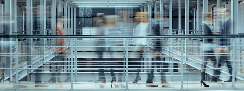Verschwommene Menschen, die durch ein modernes Gebäude mit Glas- und Stahlarchitektur gehen.