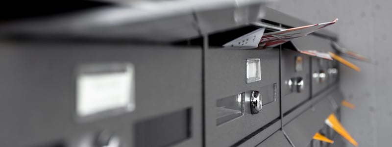 Mehrere schwarze Briefkästen, aus deren Schlitzen Briefe und Zeitschriften ragen.