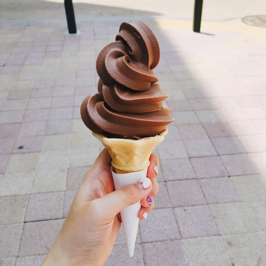 Schoko-Softeis in der Hand auf sonniger Straße – Symbolbild Ferienjob im Sommer