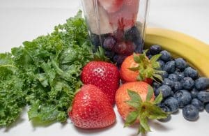 Mixer mit Erdbeeren, Blaubeeren, Banane und Gruenkohl