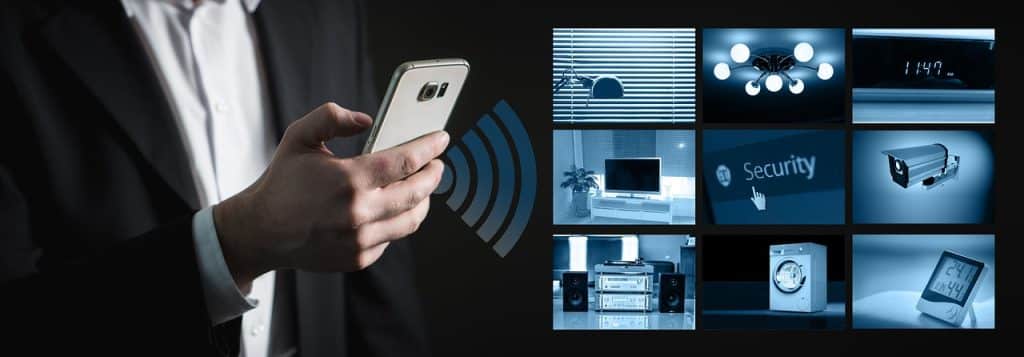 Hand mit Smartphone vor Bildschirmen einer Hausüberwachung