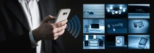 Hand mit Smartphone vor Bildschirmen einer Hausüberwachung